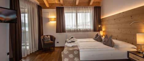 Habitación de hotel con techo de madera, una cama con almohadas, una silla, un televisor y una mesita de noche con una lámpara.