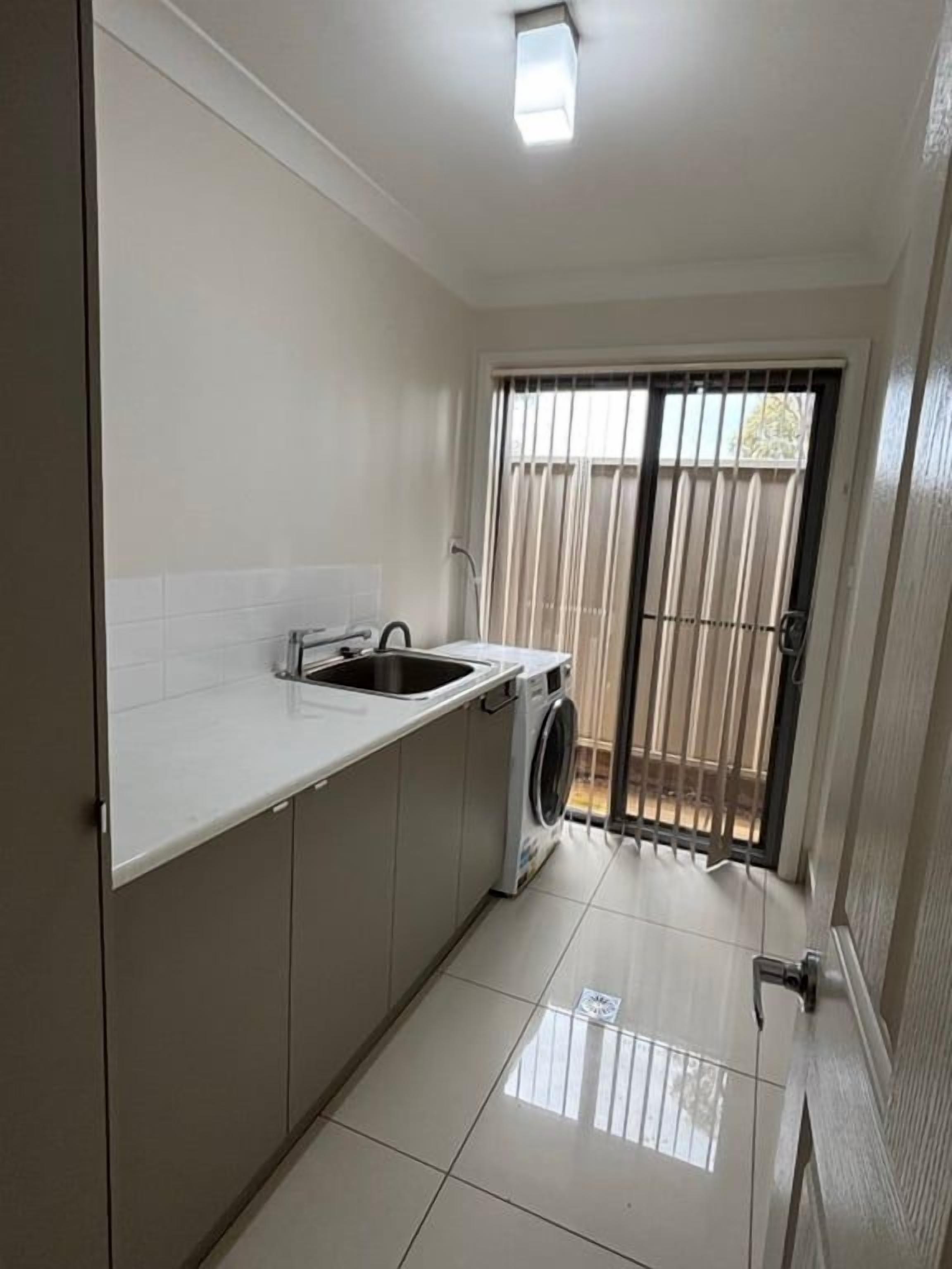 A compact kitchen with a sink, washing machine, and a window with blinds.
