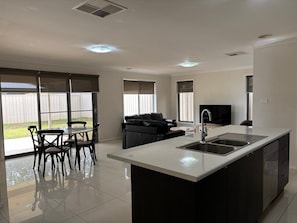 A modern kitchen with a central island, a dining area with chairs, a sofa, and a television. - St Pauls Two (Wagga Wagga)