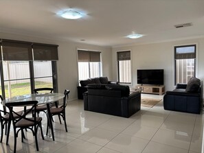 A spacious living room with a glass dining table, two sofas, a flat-screen TV, and large windows. - St Pauls Two (Wagga Wagga)
