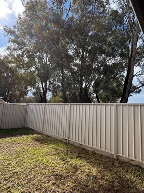 A fenced backyard with grass and trees.