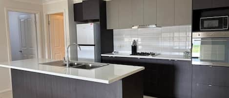 A modern kitchen with a central island, stainless steel appliances, and dark cabinetry.