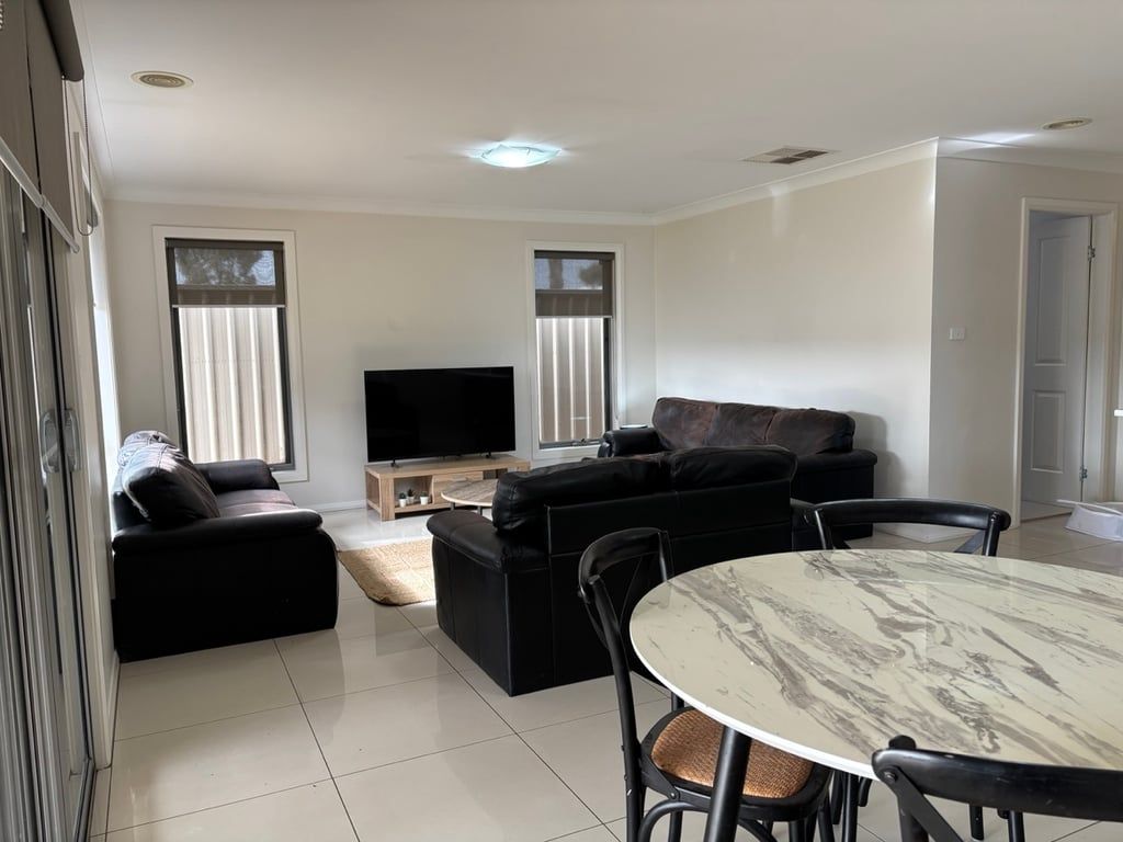 A modern living room with a black sofa set, a flat-screen TV, and a marble table.