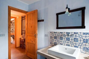A bathroom with a white sink, a wooden door, and a tiled wall with a floral pattern. - Palmento Monterosso (Trecastagni)