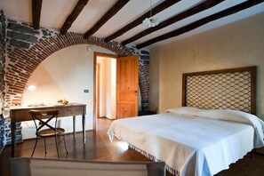 Un dormitorio con un arco de piedra, un escritorio de madera, una cama con cabecera y una puerta que da a otra habitación.