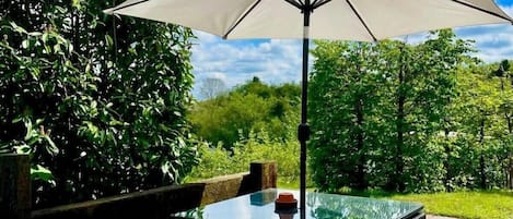 A hot tub with a table and umbrella in a garden setting.