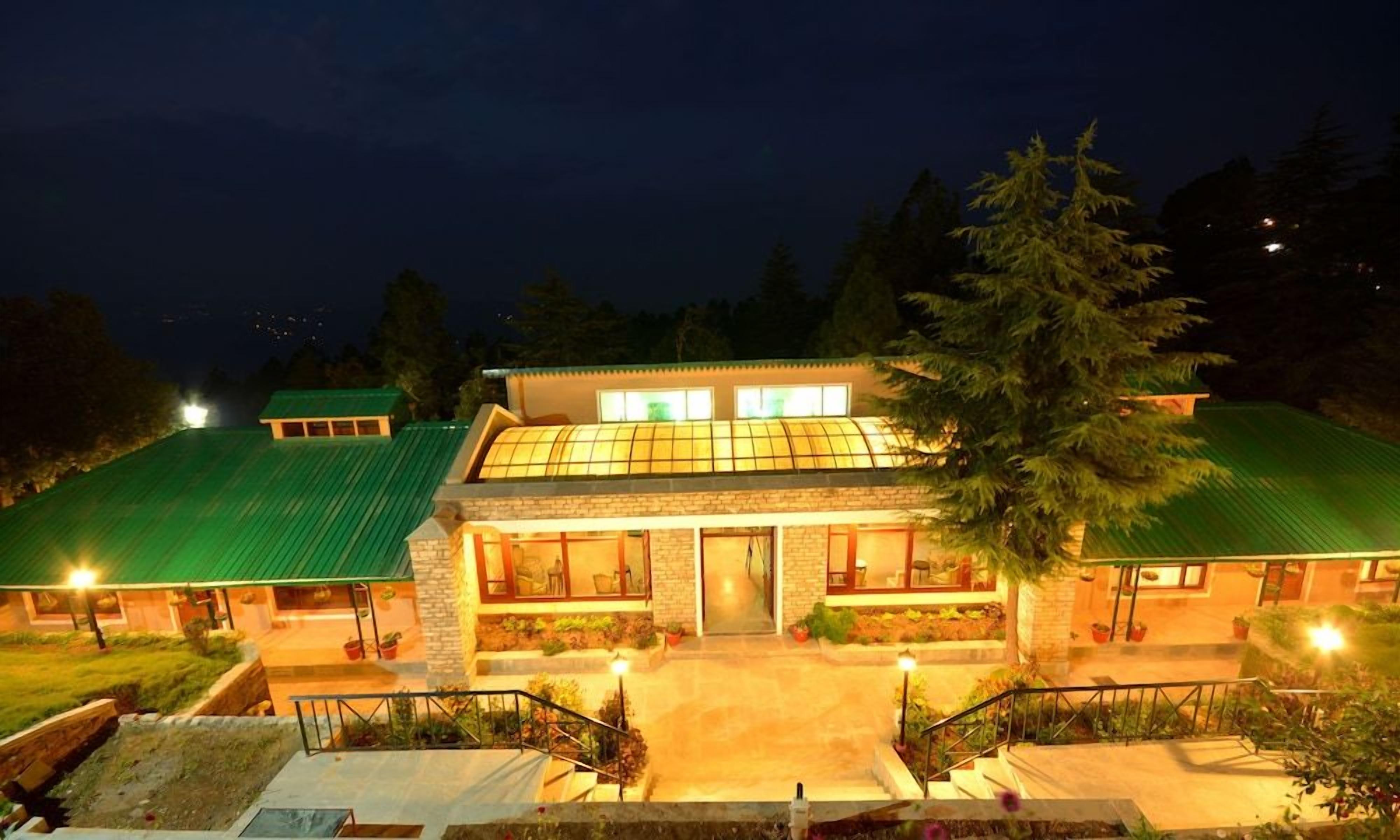 A hotel with a green roof, a glass conservatory, and a well-lit entrance.