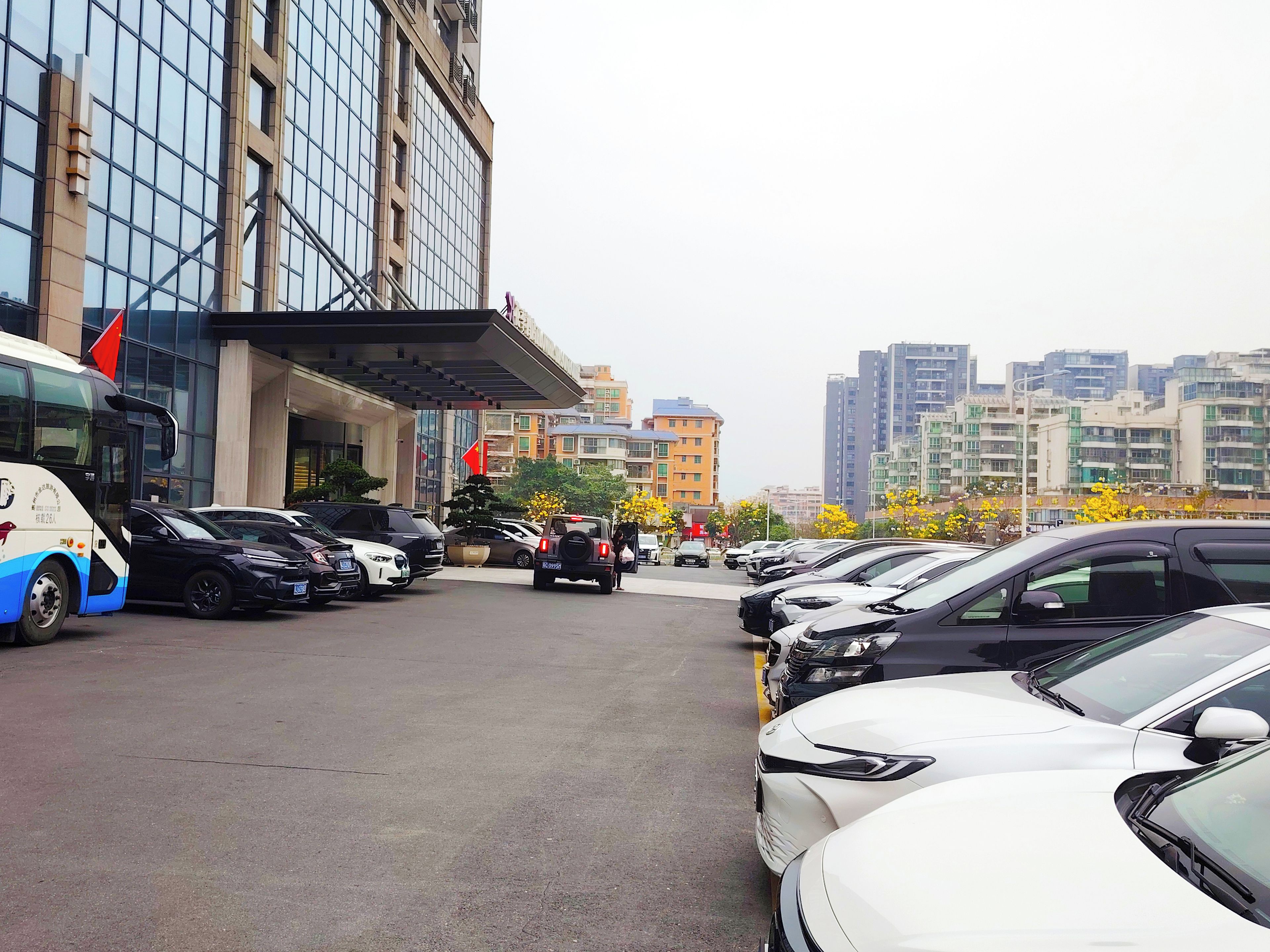 A parking lot with multiple cars and a bus, a building with a glass facade, and a clear sky.