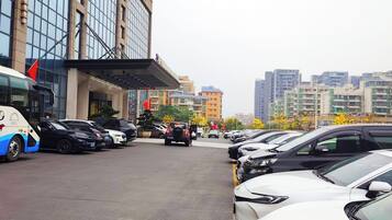 A parking lot with multiple cars and a bus, a building with a glass facade, and a clear sky.
