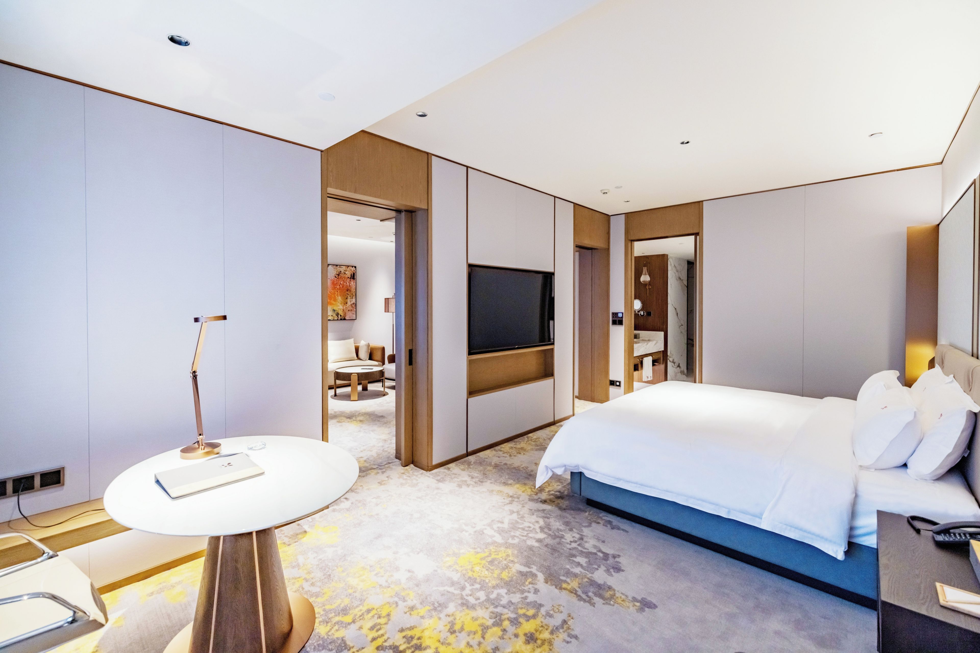 A modern hotel room with a bed, a desk, a chair, a TV, and a bathroom.