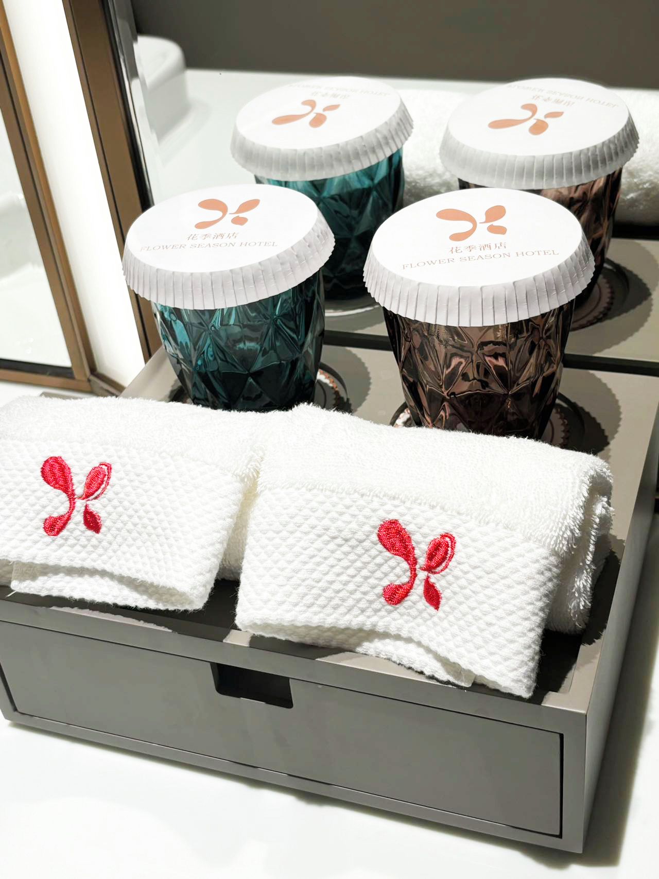 A set of toiletries in a hotel drawer, including a white towel with a red bow and a bottle with a white cap.