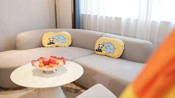 A modern living room with a beige sofa, two yellow pillows with cartoon animals, and a white coffee table with a fruit bowl.