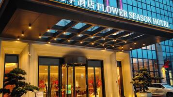 Ein Hotel mit Glasfassade, einem Schild mit der Aufschrift 'Flower Season Hotel' und einem geparkten Auto davor.