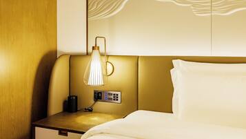 A hotel room with a bed, a bedside table with a lamp, and a wall panel.