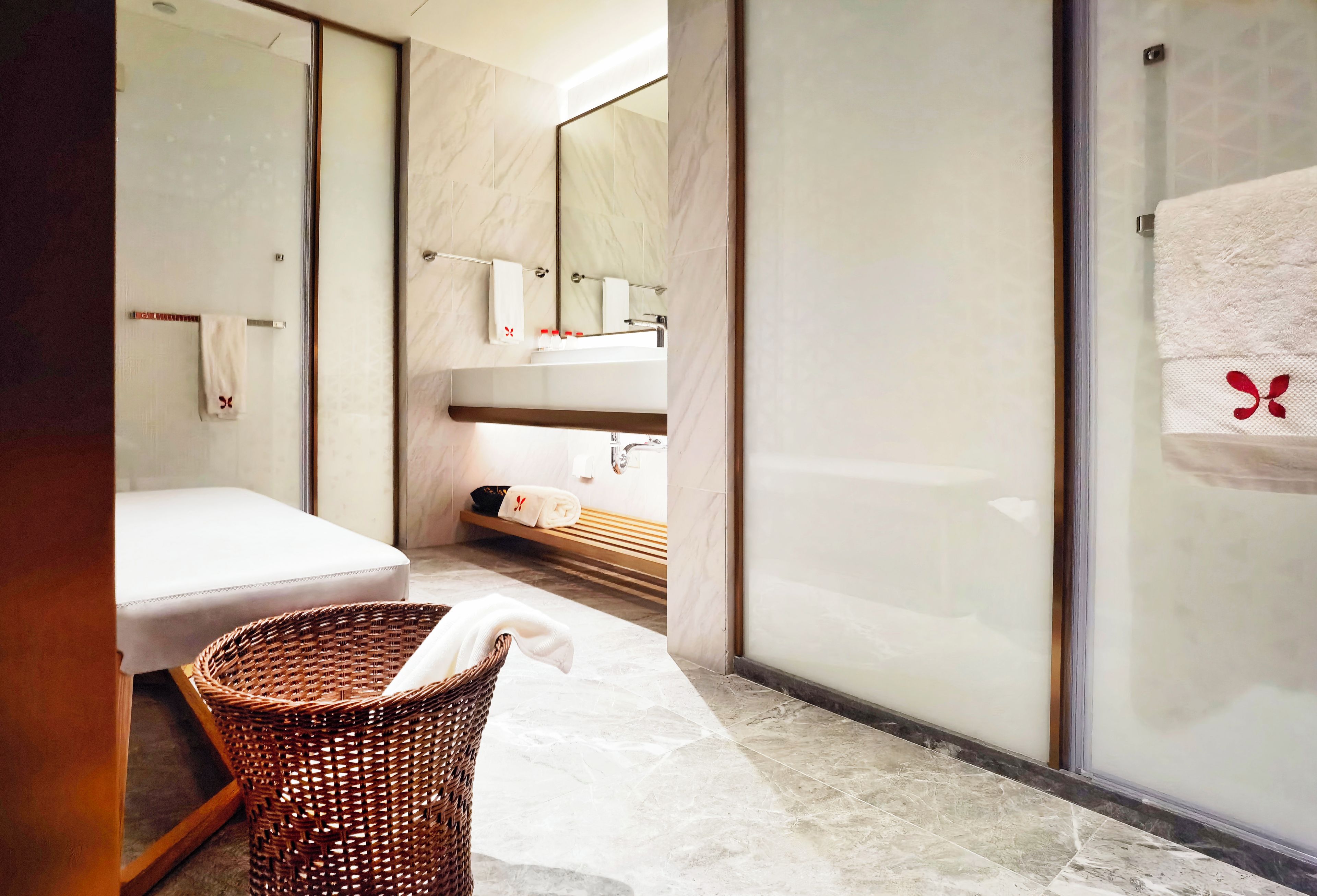 A modern bathroom with a large mirror, a white sink, and a wicker basket.