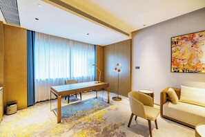 A hotel room with a desk, chair, sofa, and a large abstract painting on the wall. - Flower Season Hotel (Jiangmen)