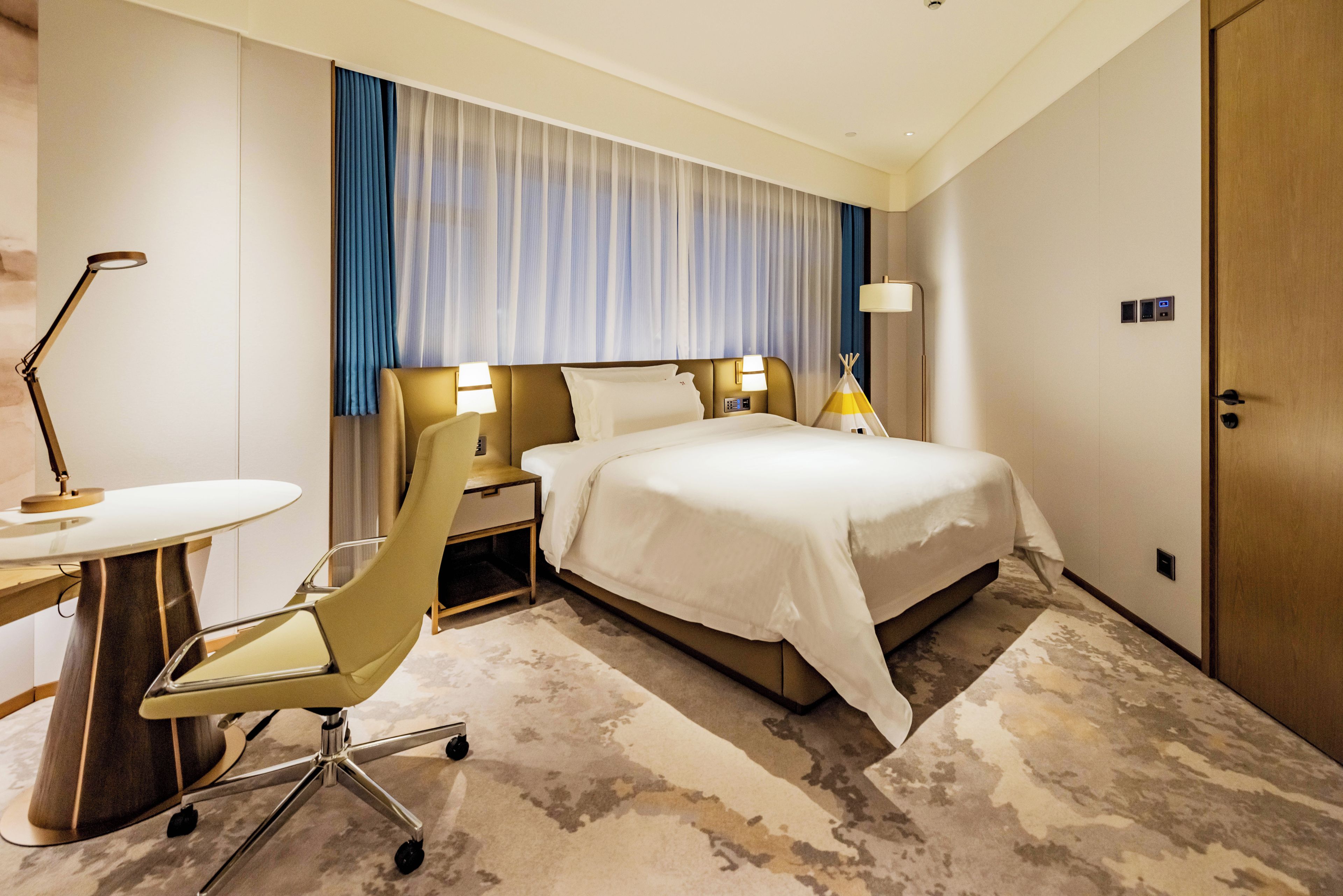 Una habitación de hotel con cama, mesitas de noche, escritorio, silla y puerta.
