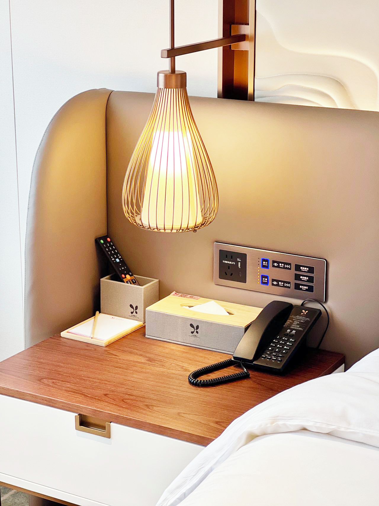 A hotel room with a bedside table, a lamp, a telephone, and a remote control.