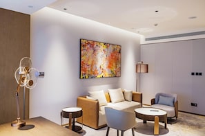 A modern hotel room with a sofa, two armchairs, a coffee table, a floor lamp, and a large abstract painting on the wall. - Flower Season Hotel (Jiangmen)