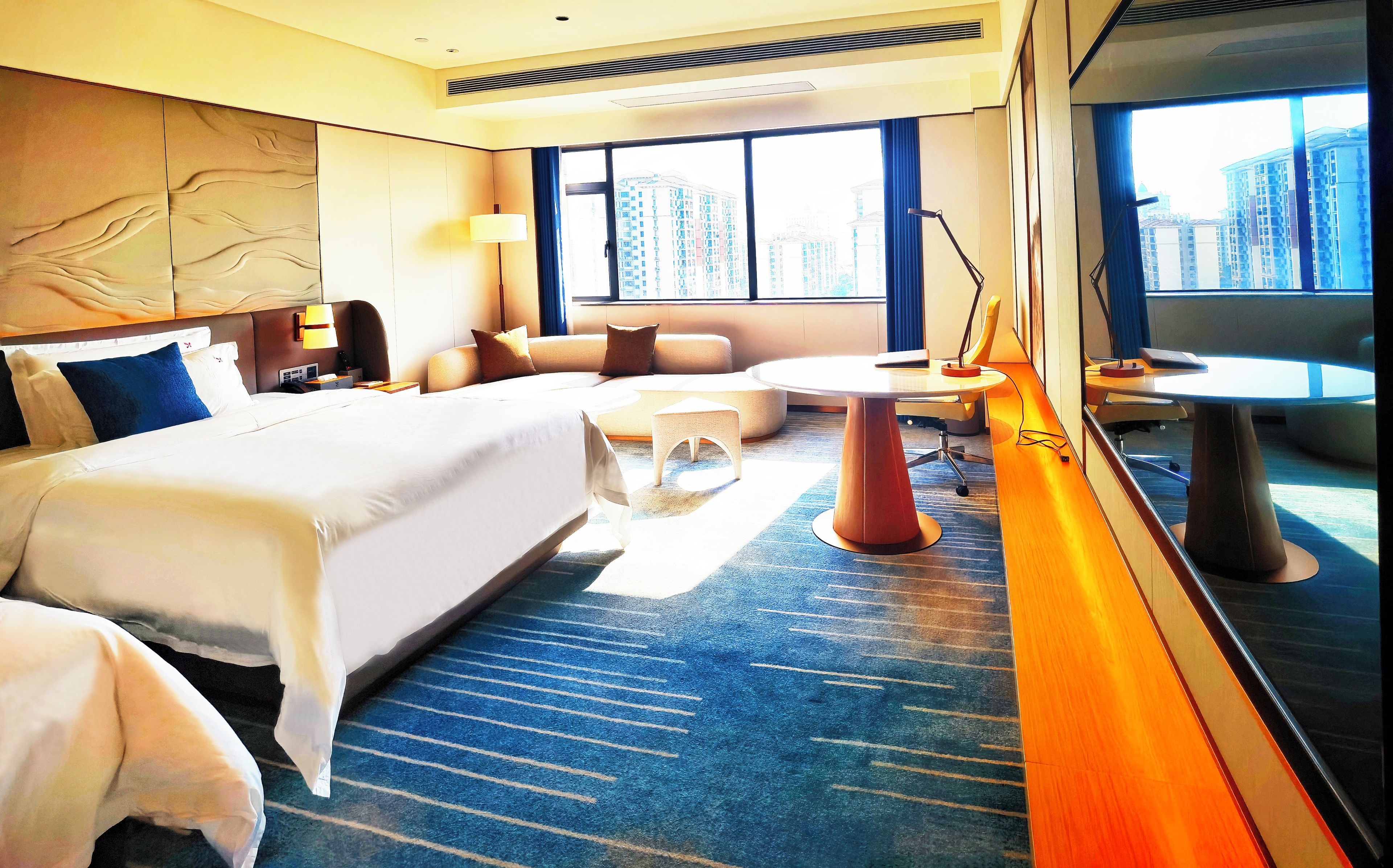 A hotel room with a large bed, a seating area, a small table, and a view of tall buildings.