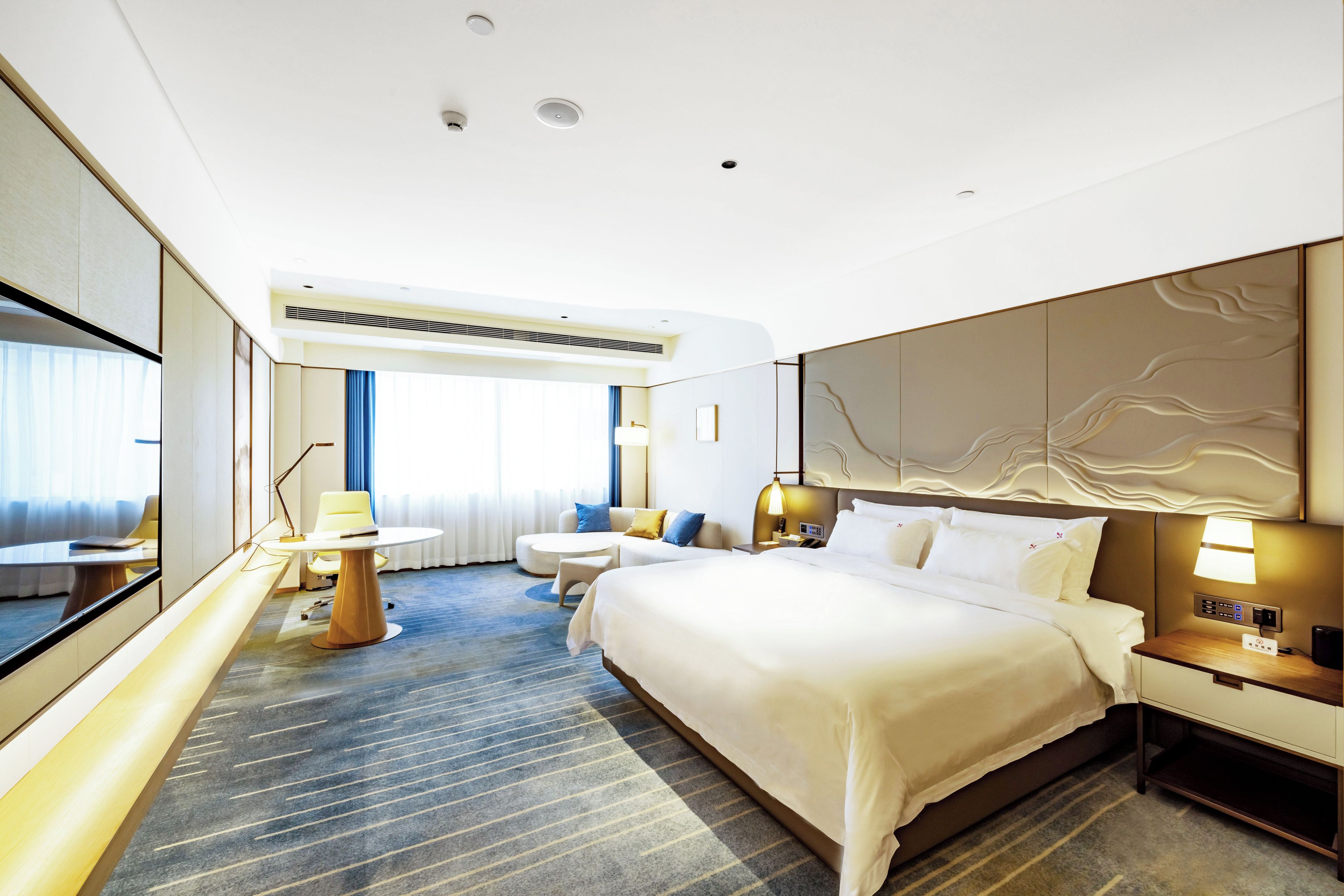 Ein modernes Hotelzimmer mit einem großen Bett, einem Schreibtisch, einem Sessel und einem Fernseher.
