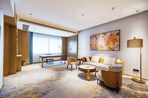 A modern hotel room with a sofa set, a dining table, and a large abstract painting.