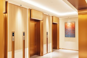 A modern elevator with a digital display, a textured wall, and a geometric art piece. - Flower Season Hotel (Jiangmen)