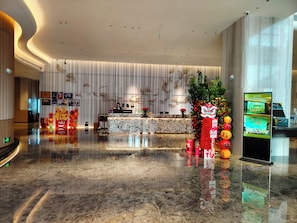 A hotel lobby with a reception desk, a digital screen, and a decorative plant. - Flower Season Hotel (Jiangmen)