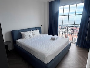 A hotel room with a large bed, a small table, and a view of the city through a window. - MINH PHUNG PHU QUOC (Phu Quoc)