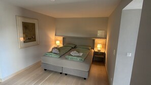 A small bedroom with a bed, two bedside tables with lamps, a framed picture on the wall, and a wooden floor.