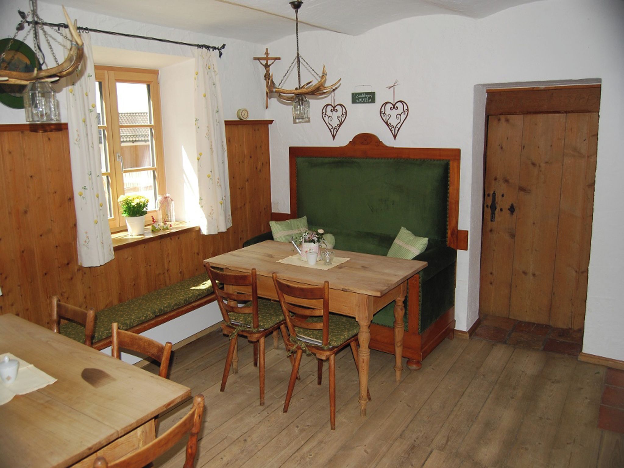 A cozy dining area with a wooden table and chairs, a bench with cushions, and a green upholstered headboard.
