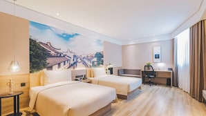 Camera d'albergo con due letti, una scrivania, una sedia e un grande murale sulla parete.