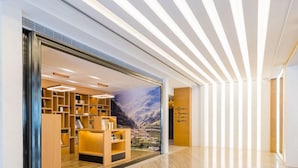 A modern hotel lobby with a wooden reception desk, a large mural of a mountainous landscape, and a sleek, light-colored floor. - Atour Hotel (Nanjing)
