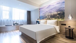 Habitació d'hotel moderna amb un llit gran, vista a les muntanyes a través d'un mural i una taula petita amb una làmpada.