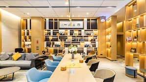 Rebost modern d'hotel amb una llarga taula de recepció de fusta, cadires blaves, un sofà amb coixins estampats i una prestatgeria plena de llibres i objectes decoratius.