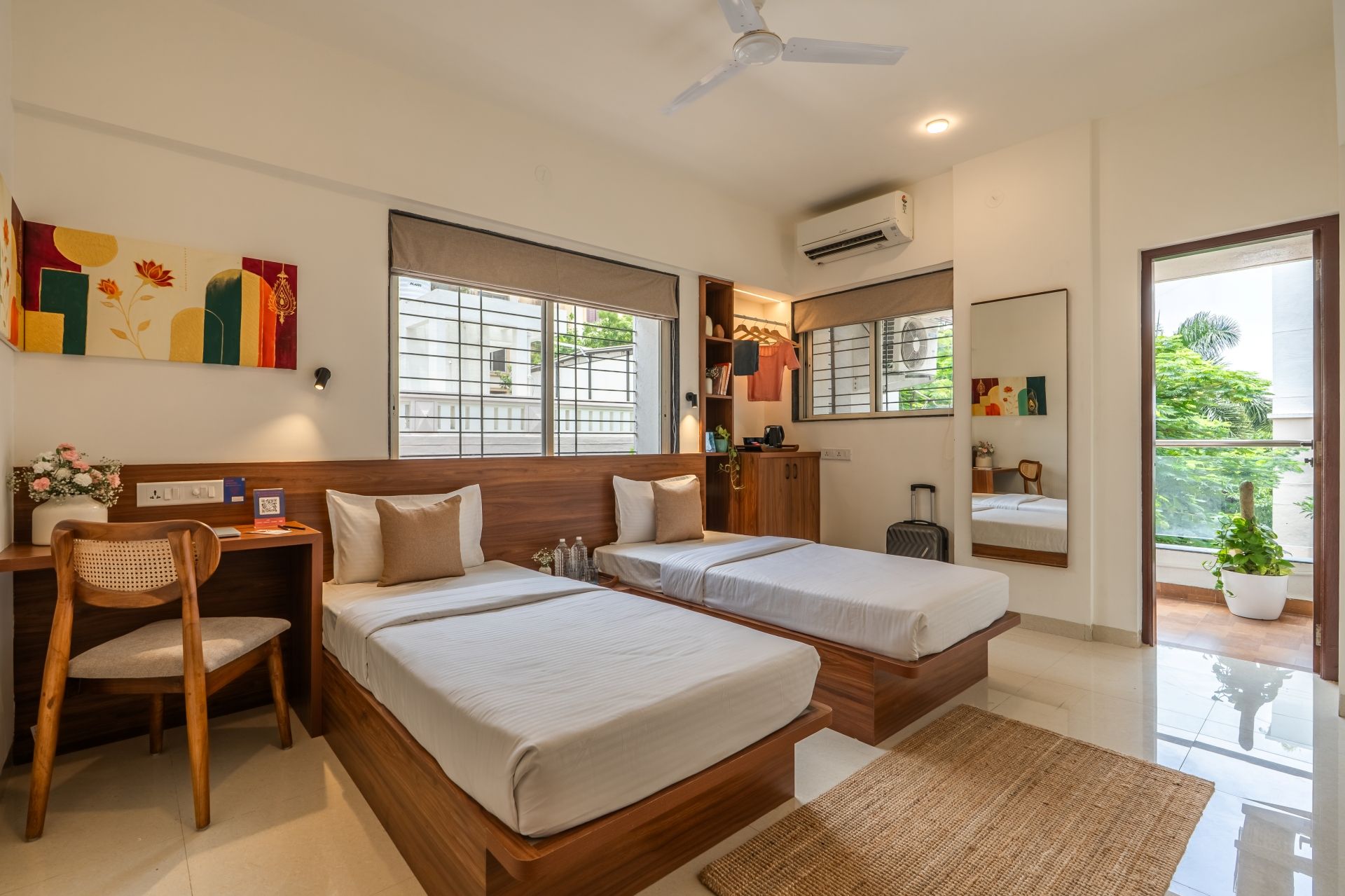 A hotel room with two beds, a desk, a chair, and a large window.