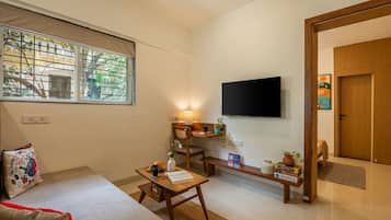A living room with a sofa, a coffee table, a TV mounted on the wall, and a window with a view of greenery.