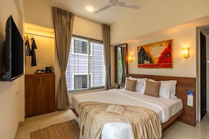 A hotel room with a bed, a television, a window with curtains, a painting on the wall, and a ceiling fan.