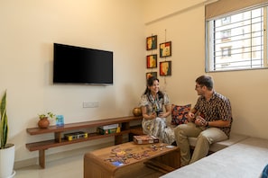 A living room with a flat-screen TV, a coffee table with puzzle pieces, and a window with a view of buildings.