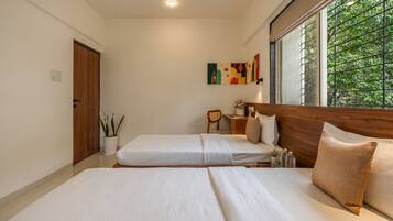 A bedroom with a large bed, a bedside table, a chair, a window with a view of greenery, and a door.