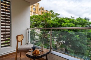 A balcony with a chair, a small table, and a view of greenery and buildings. - LiveAway Pune (Viman Nagar) by PACK (Pune)
