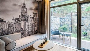 Ein modernes Wohnzimmer mit großem Fenster, einer Couch, einem kleinen Tisch und einem Stadtbild-Wandgemälde.
