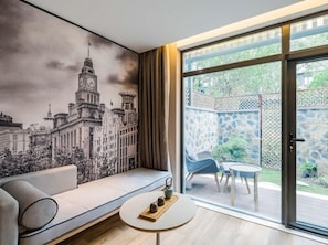 A modern living room with a large window, a sofa, a small table, and a cityscape mural on the wall. - Atour Hotel (Zhenjiang)