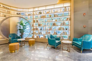 A modern library with teal chairs, a large circular mirror, and bookshelves filled with books. - Atour Hotel (Zhenjiang)