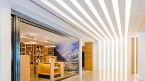 A modern hotel lobby with a wooden reception desk, a large mural of a mountainous landscape, and a sleek, light-colored floor. - Atour Hotel (Zhenjiang)