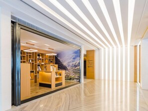 Een moderne hotellobby met een houten receptiebalie, een groot muurdecoratie van een berglandschap en een strakke, lichtgekleurde vloer.