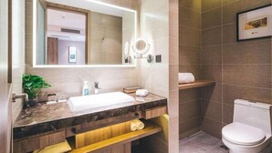 Een moderne badkamer met een marmeren wastafel, een grote spiegel met ingebouwde verlichting, een toilet en een handdoekhouder.