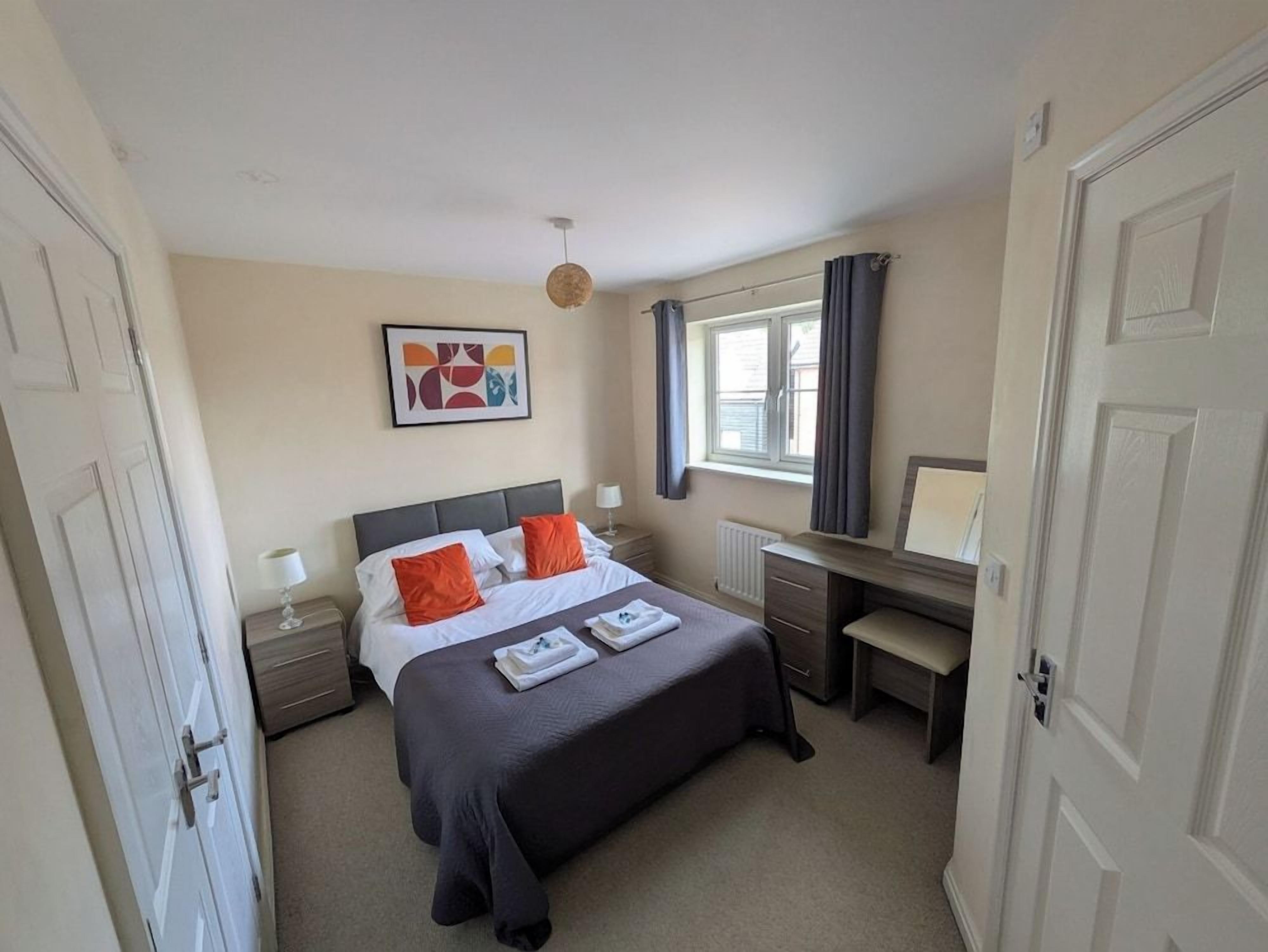 A bedroom with a bed, bedside table, lamp, and a desk with a chair.