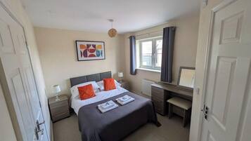 A bedroom with a bed, bedside table, lamp, and a desk with a chair.