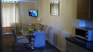 A hotel room with a dining table, chairs, a television, a mirror, and a microwave. - Thistle Cottage (Bury St Edmunds)